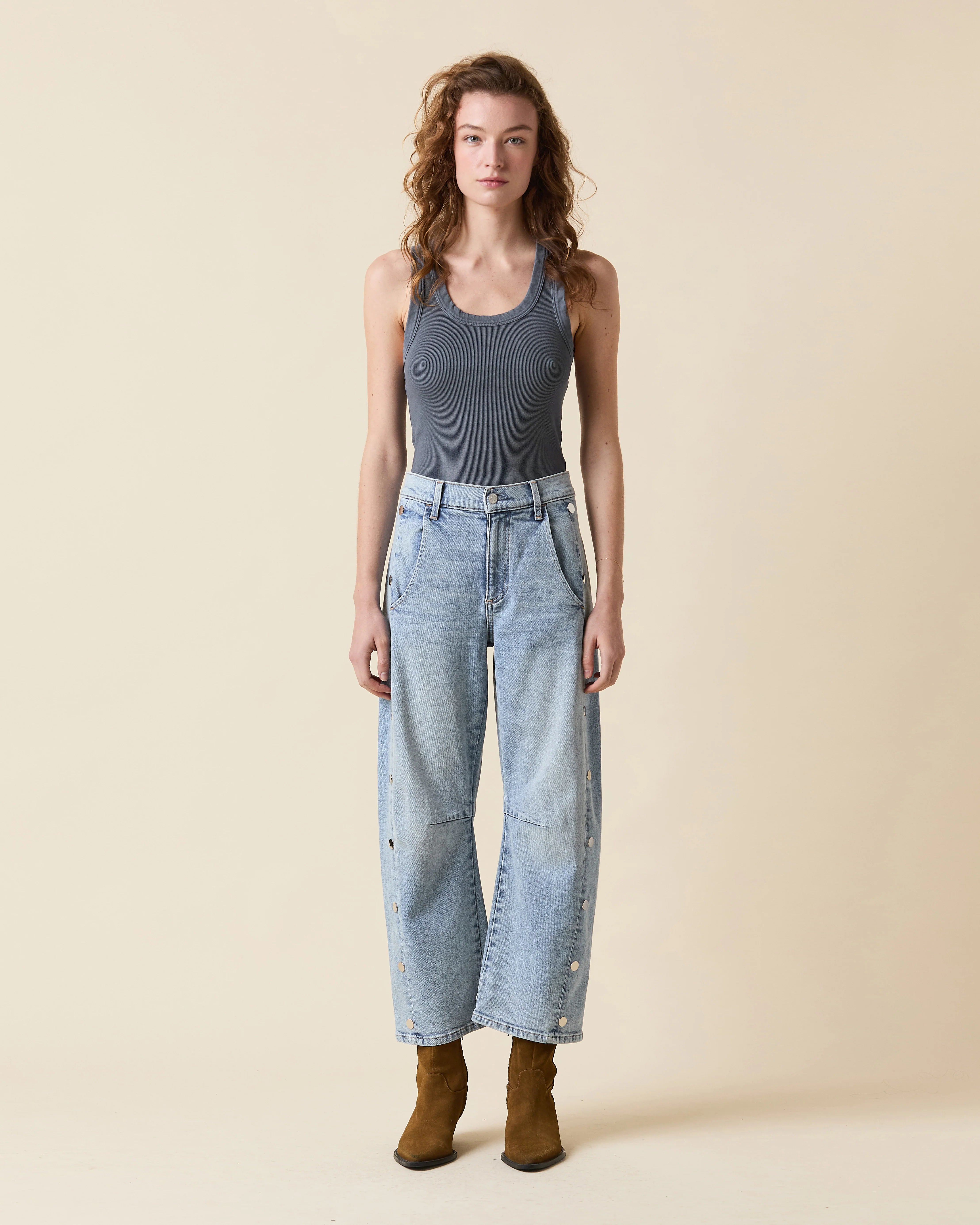 Woman wearing a gray tank top and light blue jeans against a beige background